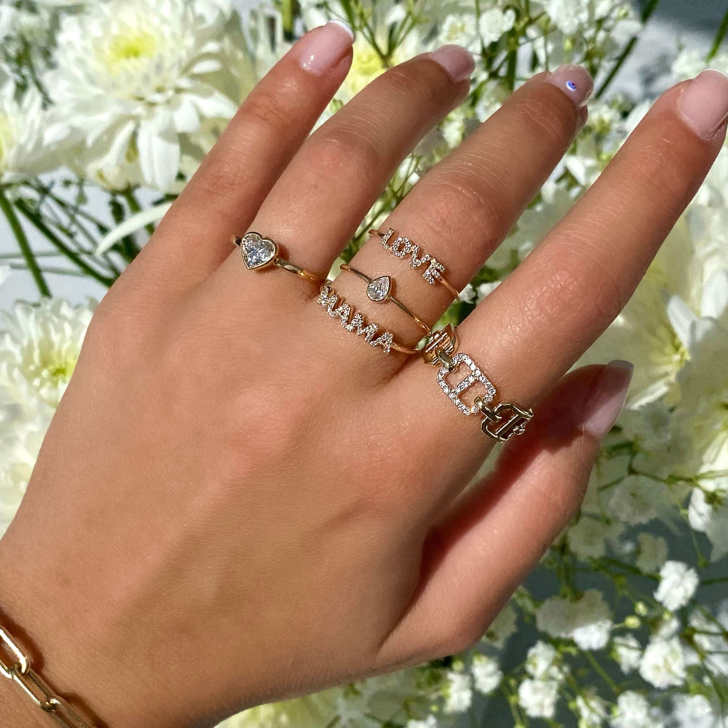 Woman's hand adorned with gold and diamond rings from our jewelry collection, surrounded by white flowers.