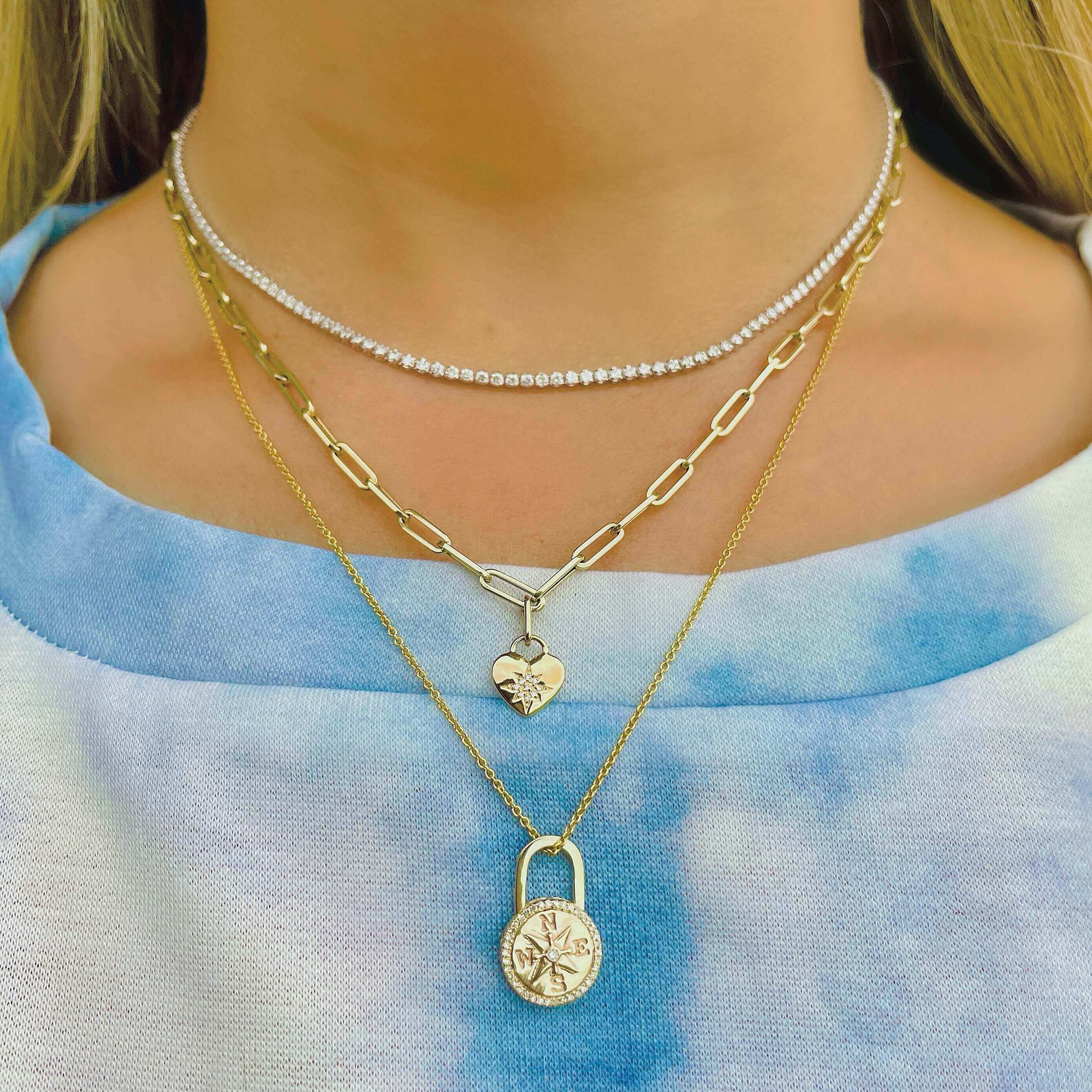 Layered gold necklaces with heart pendant and lock charm, worn with a blue gradient top.