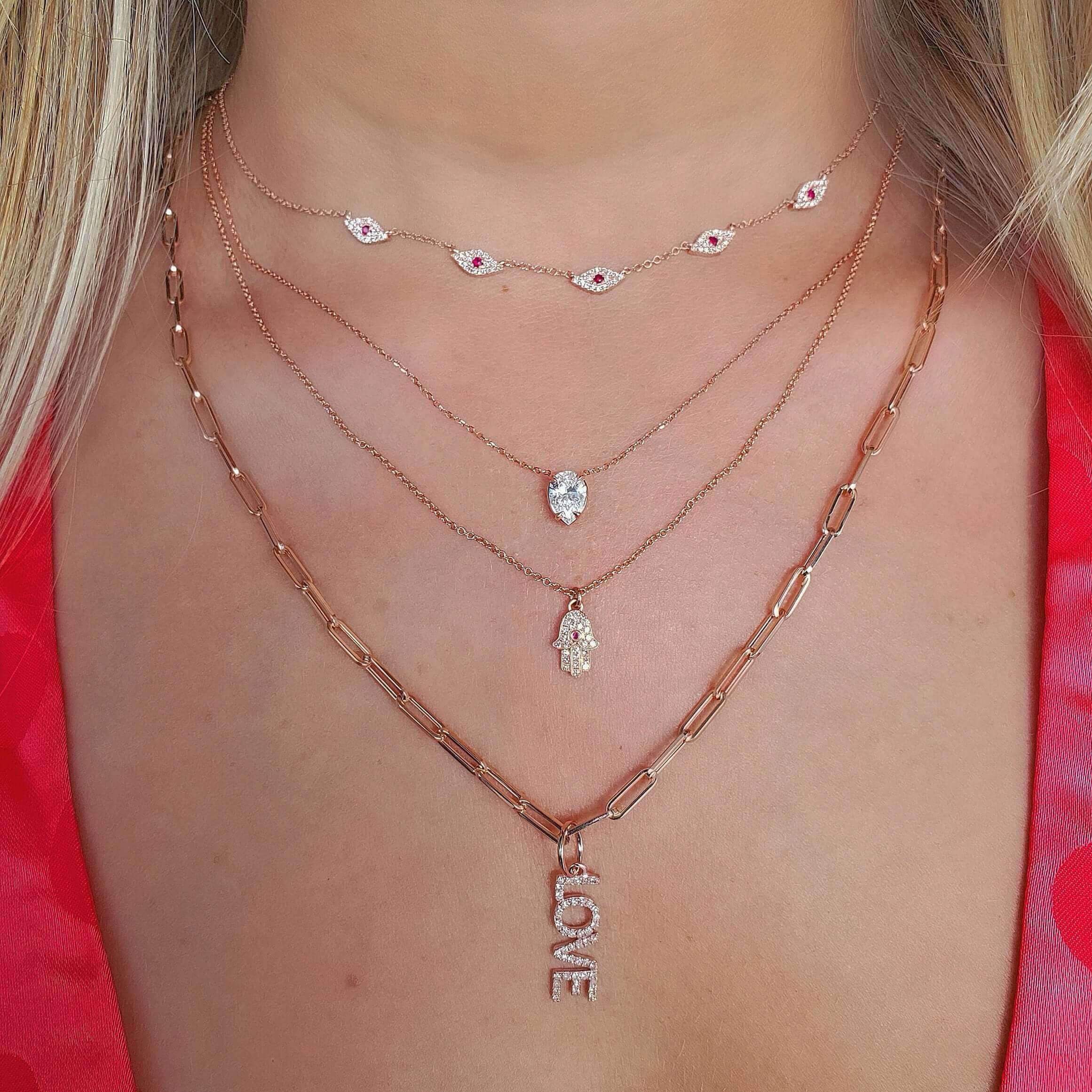 Woman wearing layered necklaces with an evil eye choker, a pendant, a hamsa charm, and a LOVE necklace from our jewelry collection