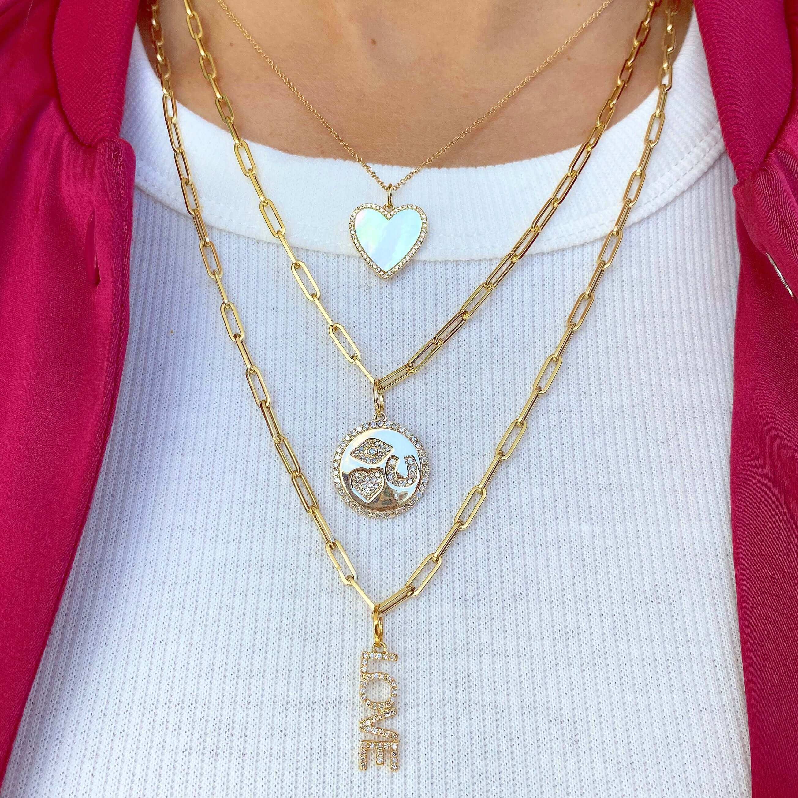 Woman wearing layered gold necklaces featuring heart, peace sign, and love pendants; showcasing elegant jewelry from our brand.