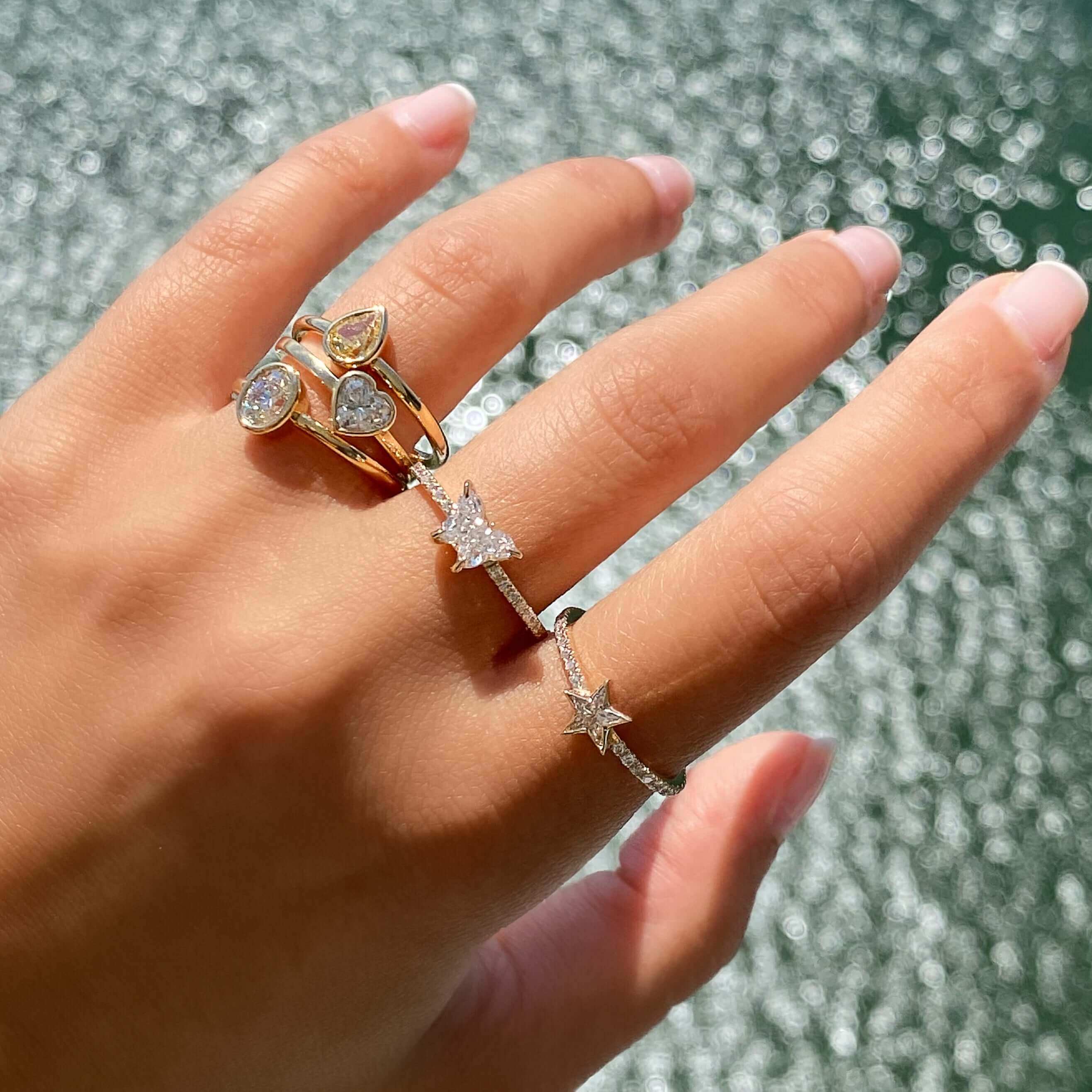 Hand wearing elegant gold and diamond rings in sunlight by the water - jewelry brand collection
