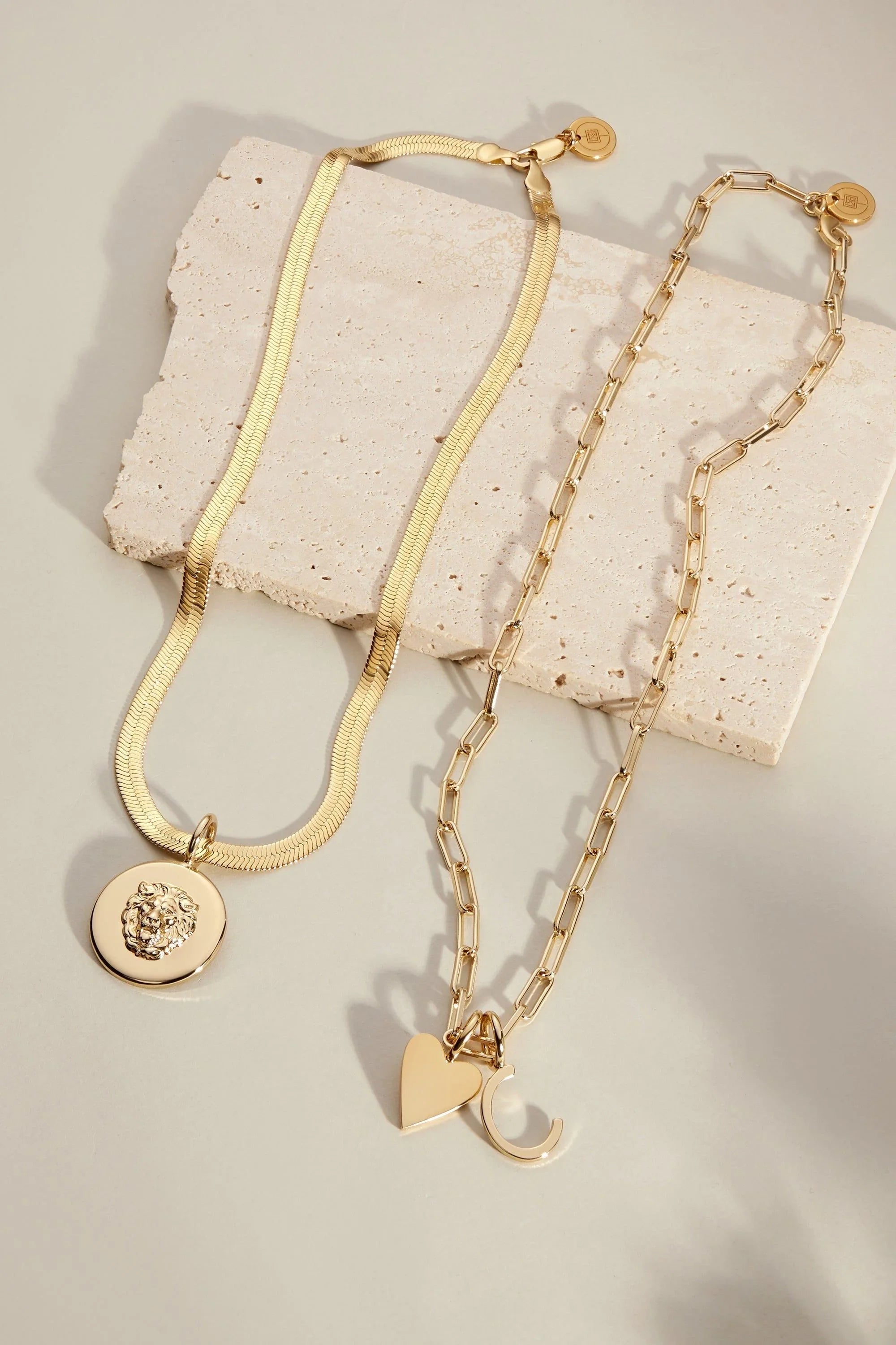 Two gold-toned necklaces from the Cara Charm Necklace collection displayed beautifully