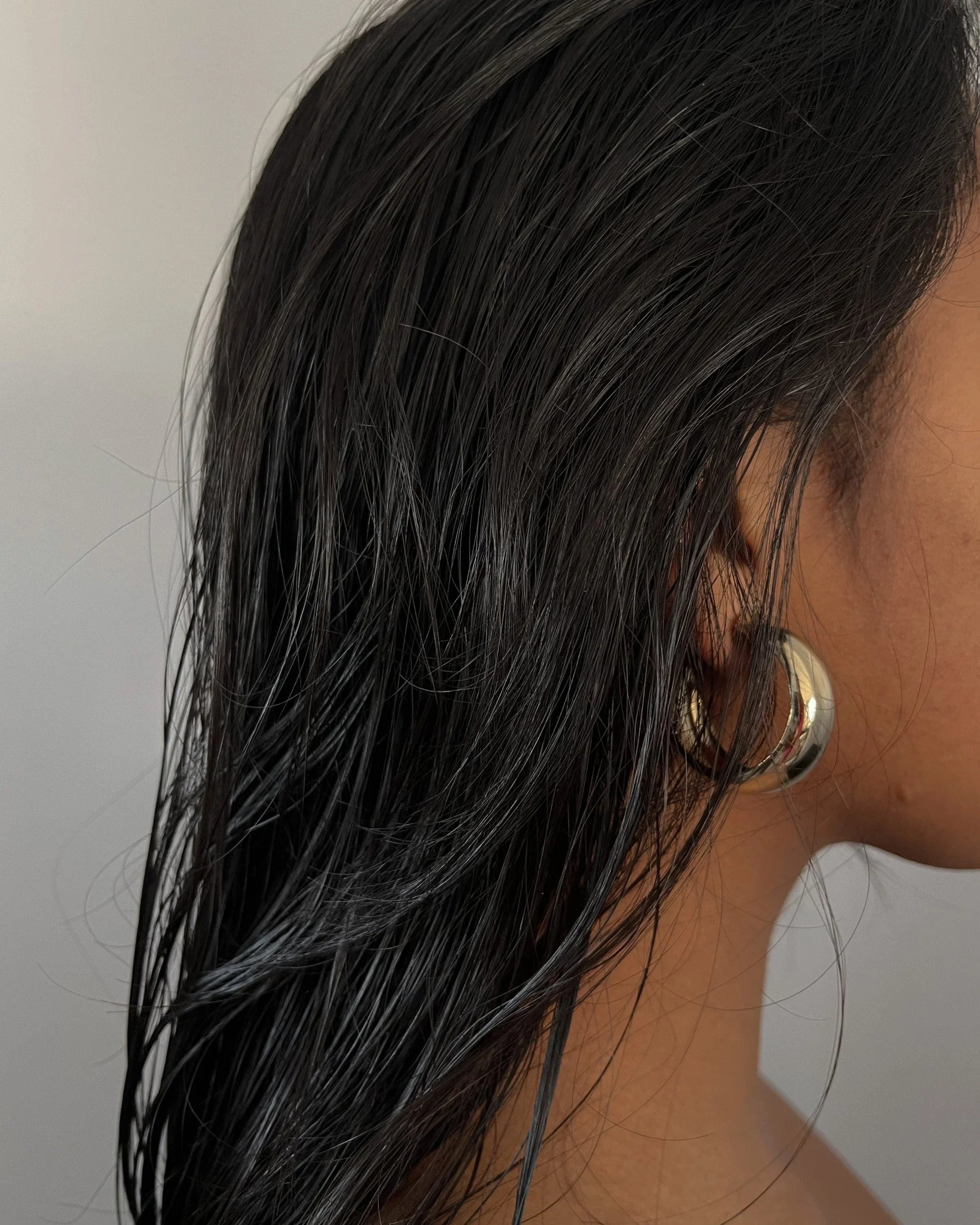 Wet dark hair with gold hoops for Simone Hoops earrings showing off style and shine