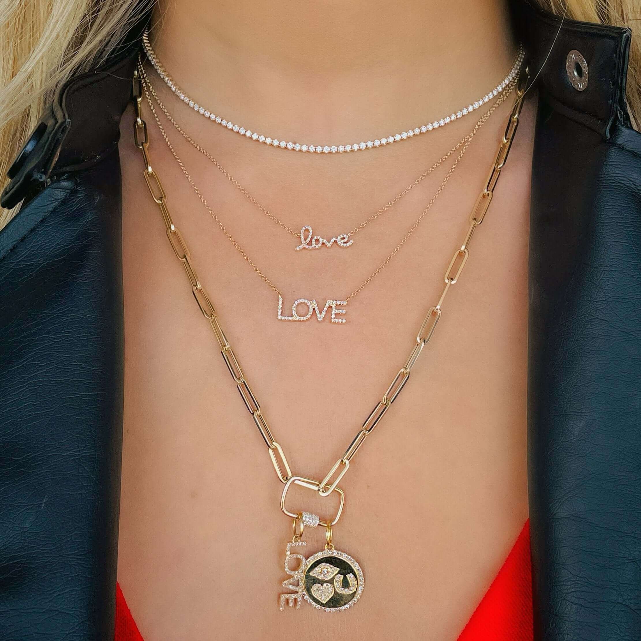 Woman wearing layered necklaces with love pendants and a stylish black jacket from our jewelry brand.