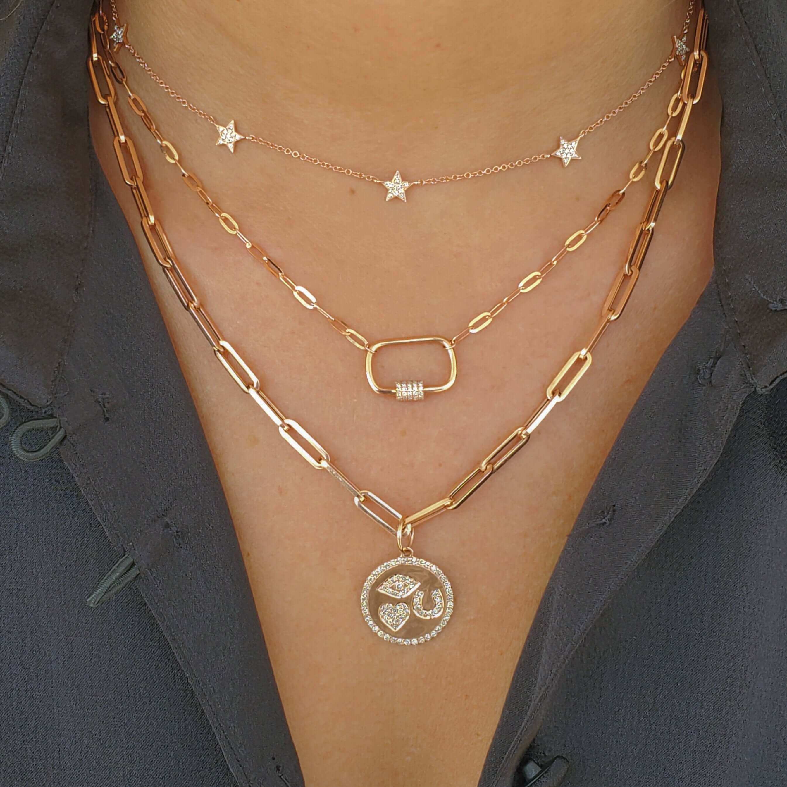 Layered gold necklaces featuring paperclip chain and star accents displayed on a model wearing a dark shirt.