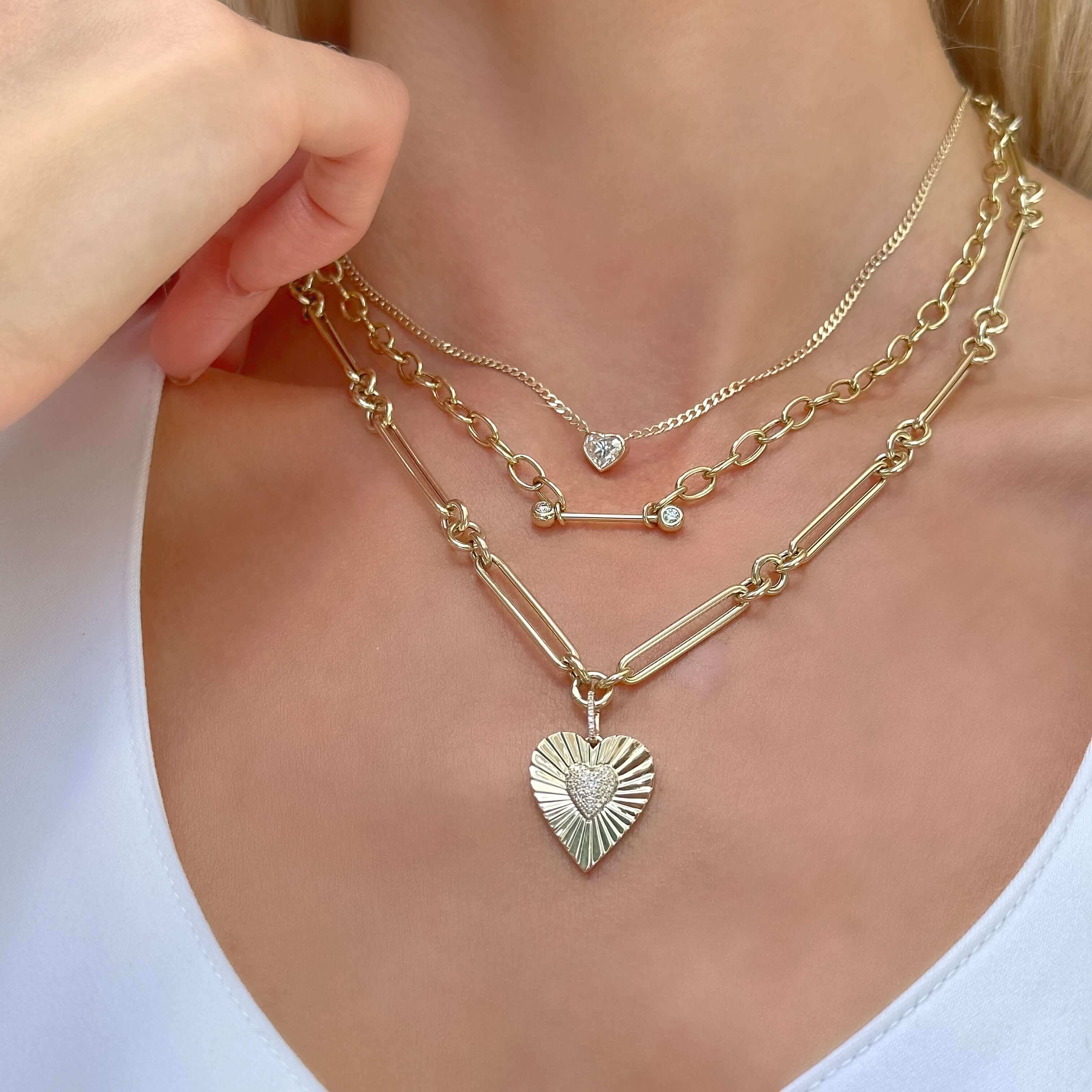 Layered gold necklaces with heart and bar pendants resting on a woman's neck, showcasing our jewelry brand's elegance and style.