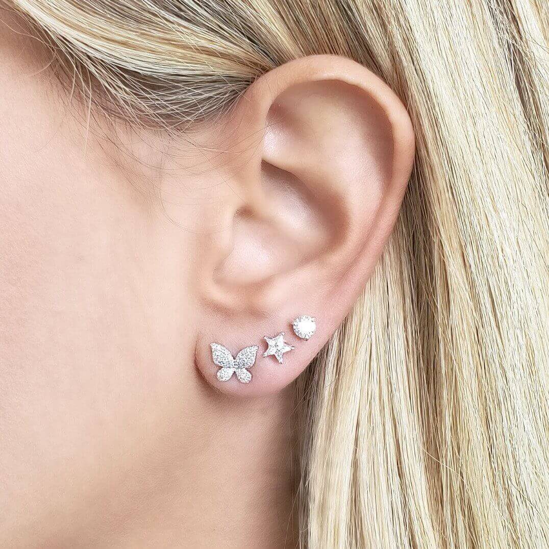 Woman wearing elegant triple stud earrings: butterfly, star, and round stud from our jewelry collection