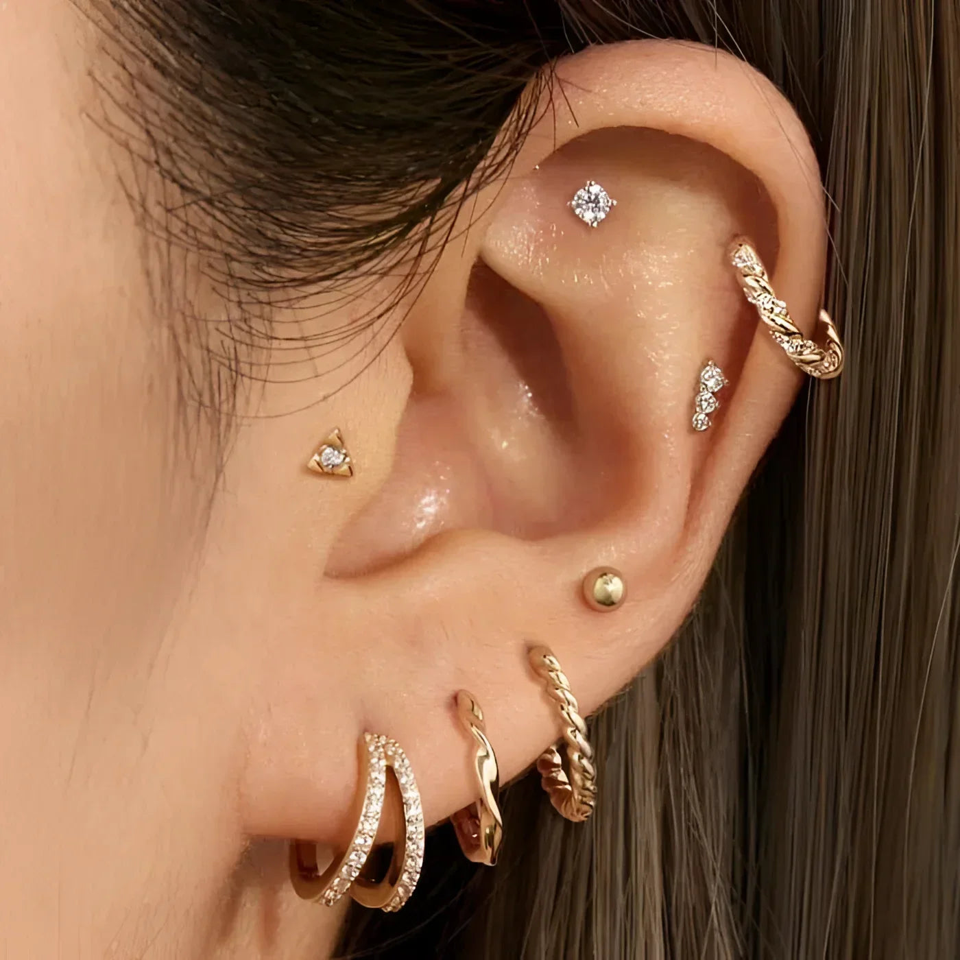 Ear with multiple gold-toned piercings wearing 14K Gold Diamond Twisted Huggie Hoops
