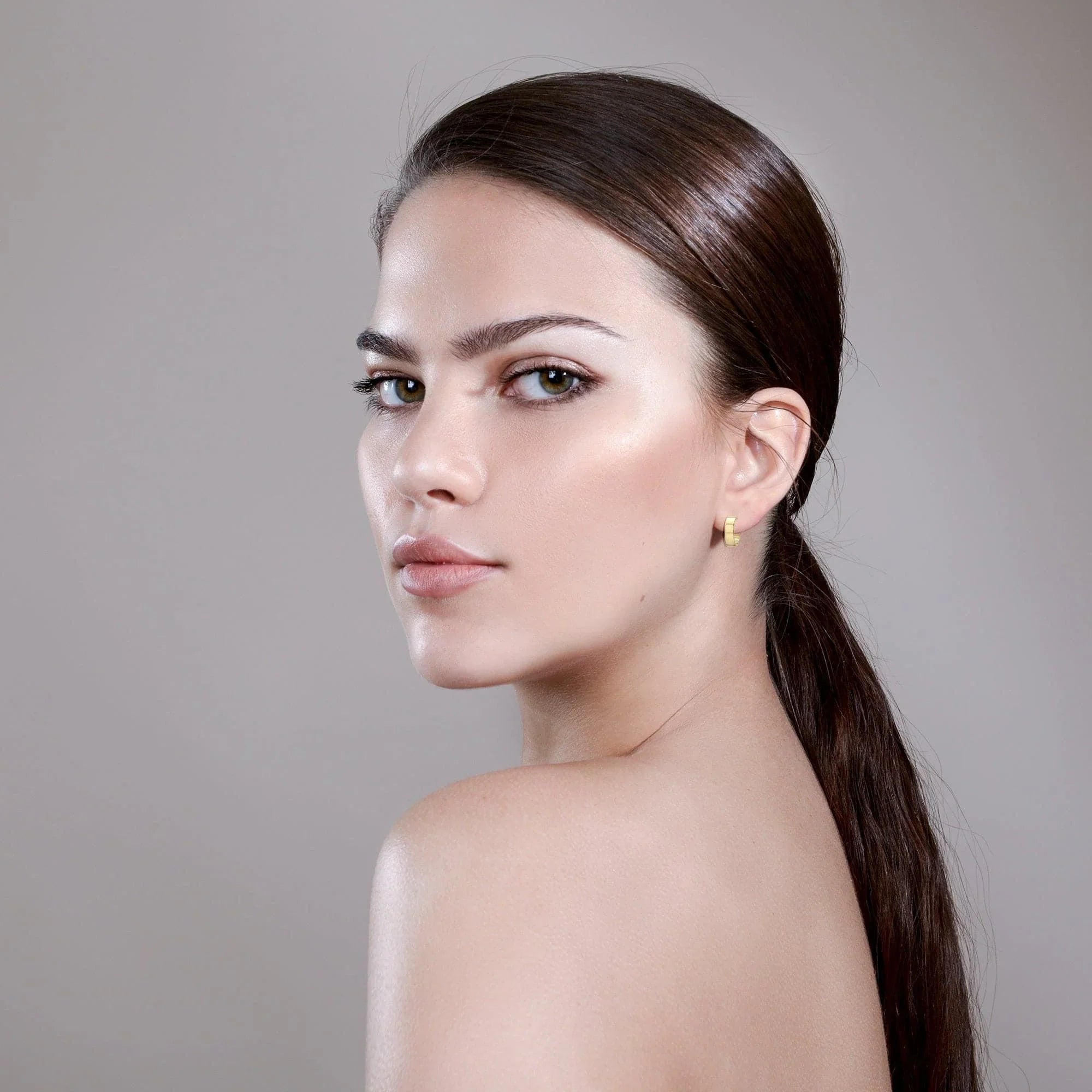Woman with sleek hair and gold earrings wearing Mini Cora Huggie Hoops
