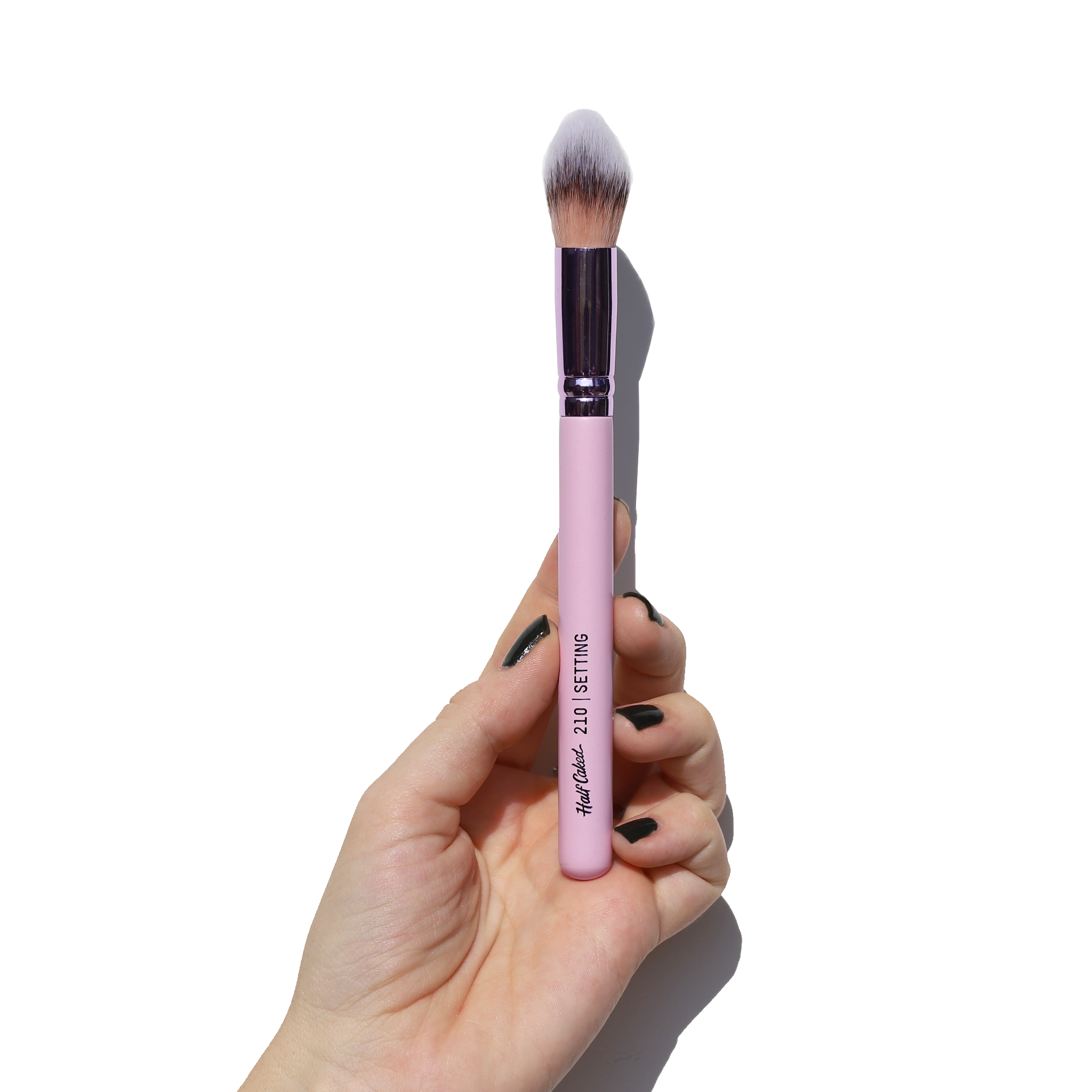 Close-up of a hand holding the 210 Setting Brush with tapered synthetic bristles for applying seamless makeup.